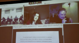A screen shows business people video conferencing with Saint Rose students during a cybersecurity class.